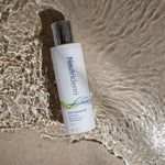 Neutriderm Anti-Dandruff Shampoo bottle on a sandy beach, capturing a lifestyle aesthetic with flowing water. 